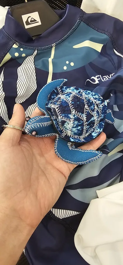 Sea turtle sewn from rashguard fabric offcuts, held in a hand above the printed fabric